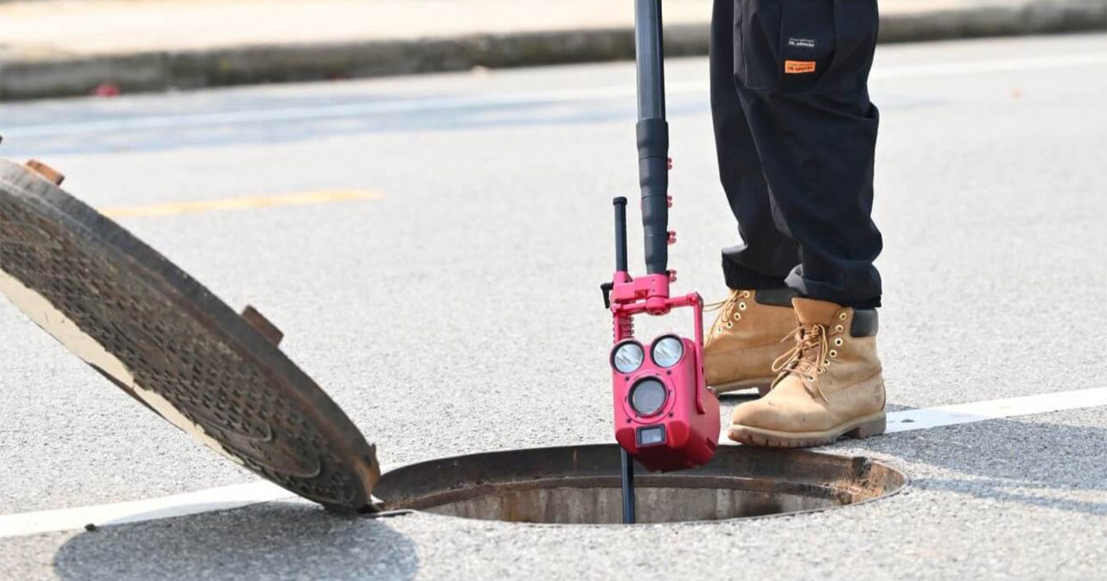 Sewer inspection camera being lowered into an open manhole in the street